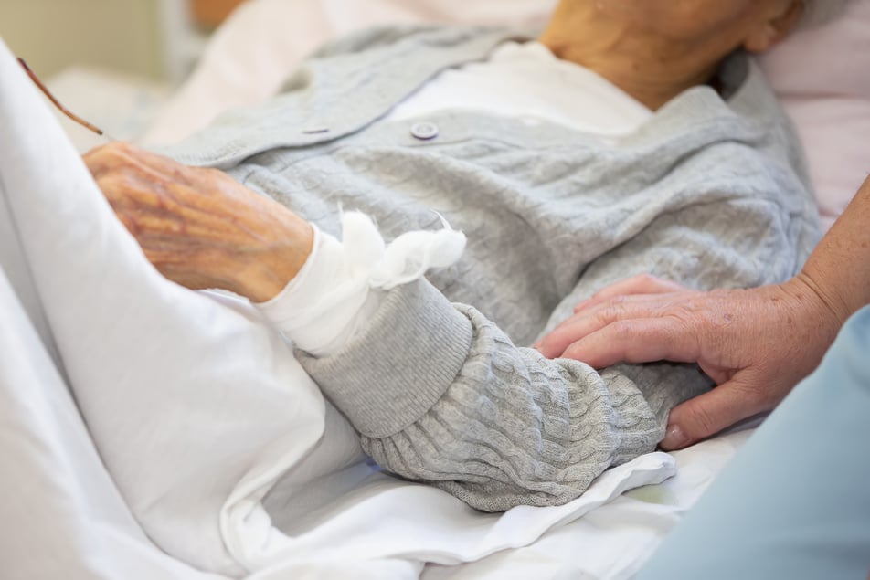 Care for an elderly bedridden sick woman. The hand of a nurse strokes the hand of an elderly infirm woman.